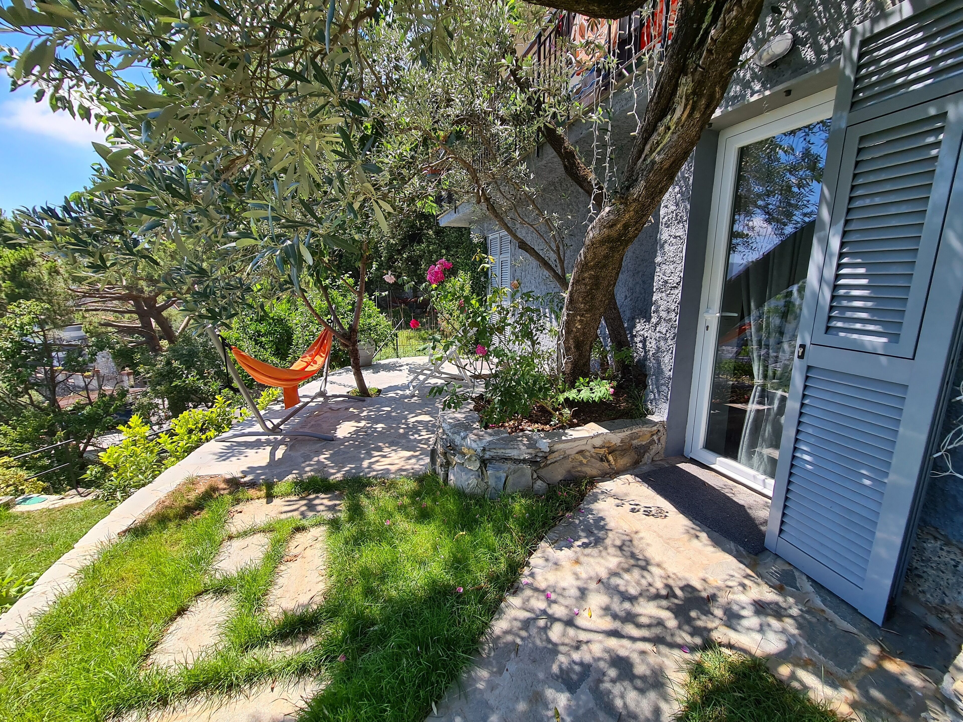 A garden with a hammock, stone pathway, and a building with a window.