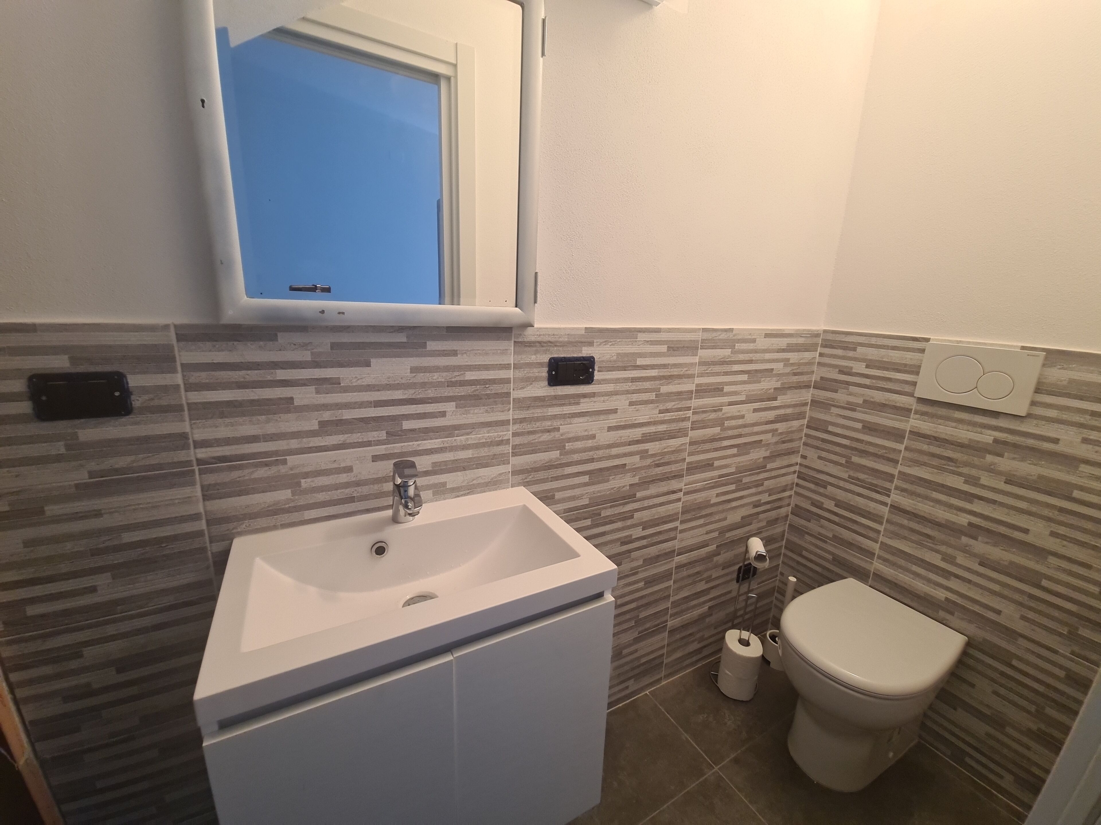 A bathroom with a white sink, a toilet, and a window above the sink.