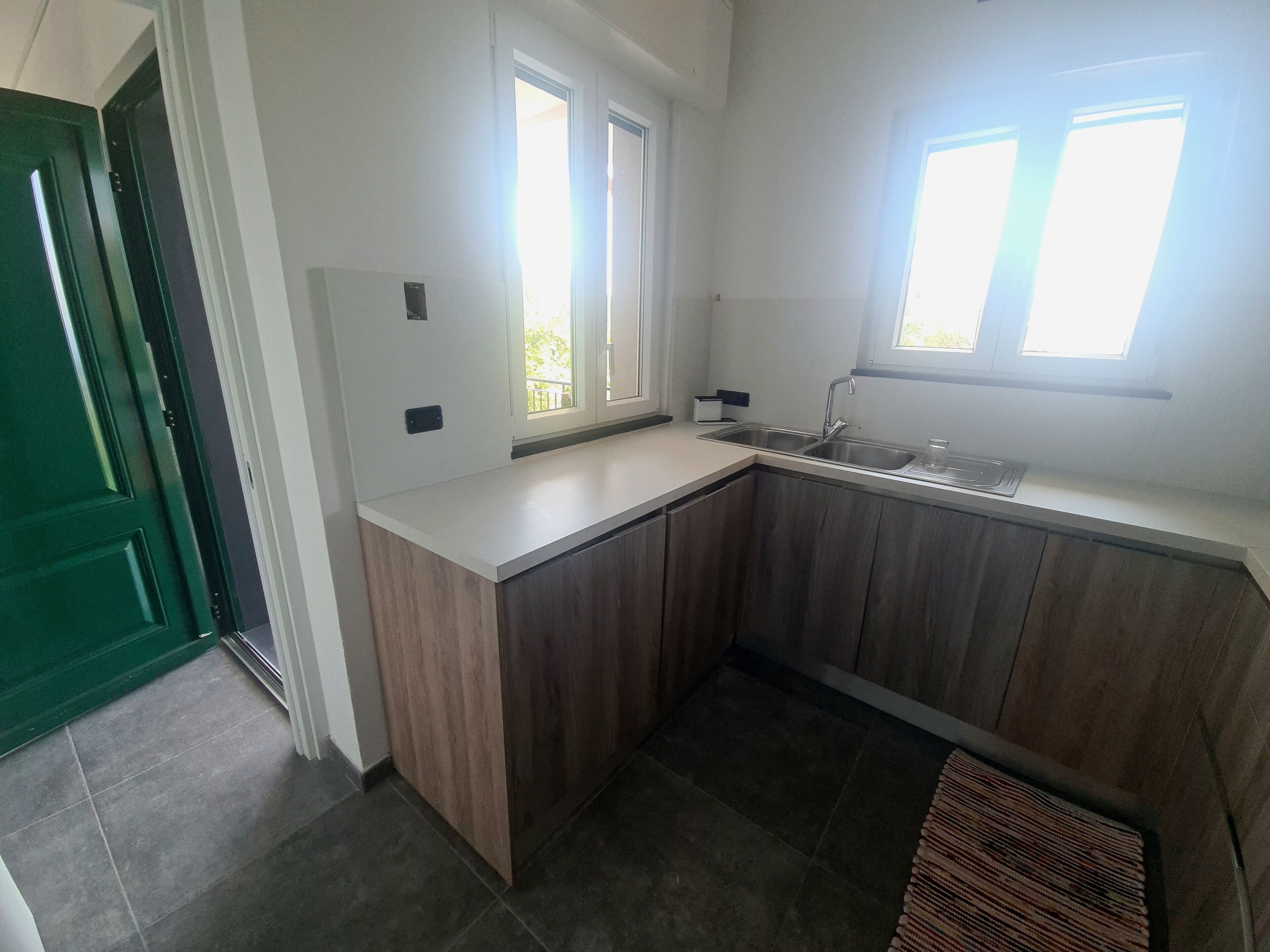 A kitchen with a white countertop, wooden cabinets, a sink, and two windows.