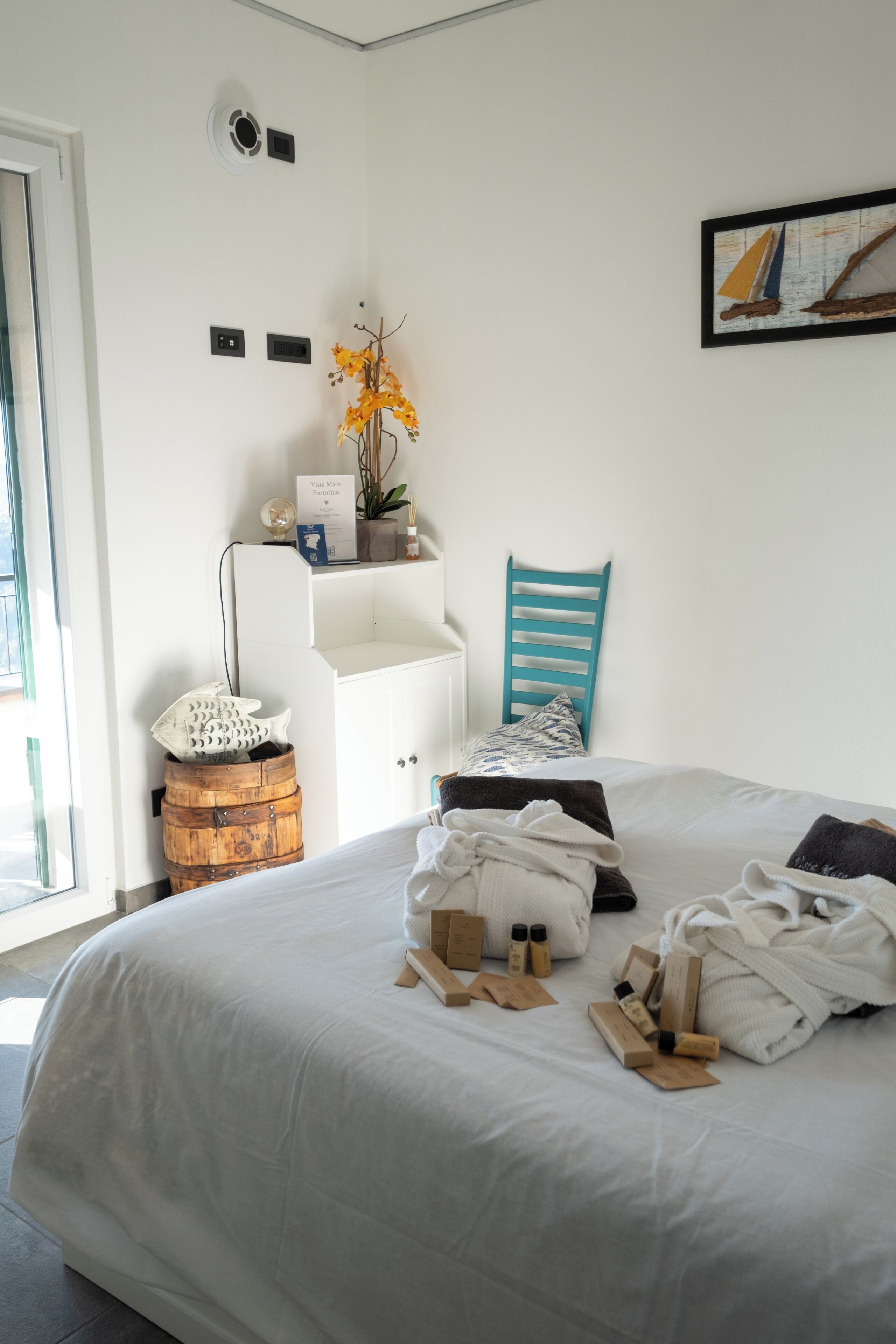 Un dormitorio ordenado con una cama, una silla, una mesita con un florero y un barril de madera.