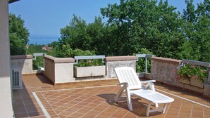 Una terraza con una silla blanca, una mesita y una maceta con flores.