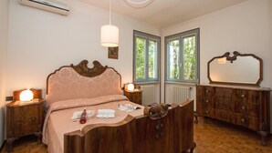 Un dormitorio con cama de madera, lámparas de noche, cómoda y ventana con vistas a la vegetación.