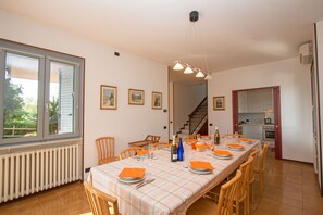 A dining area with a long table set for six, wooden chairs, a chandelier, and a view through a window. - Villa dei Salici con piscina by Wonderful Italy (Soiano del Lago)