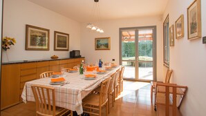 Un comedor con una mesa larga dispuesta para una comida, sillas de madera y una encimera de cocina con un lavamanos y armarios.