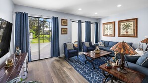 Ein modernes Wohnzimmer mit einer großen Schiebeglasdoor zum Balkon, einem blauen Sofagarnitur, einem Holztisch und zwei Sesseln.