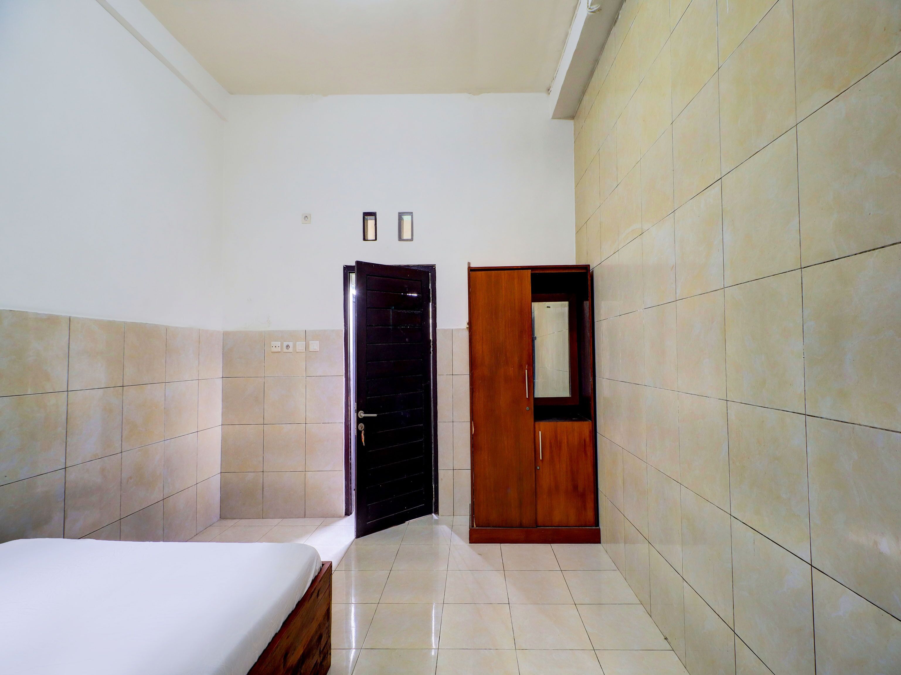 Quarto de hotel com cama, guarda-roupa e porta que dá para outro aposento.