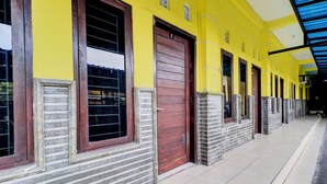 A building with a yellow facade, multiple doors, and windows with stone frames. - OYO Life 92841 Kos 88 (Perean Tengah)