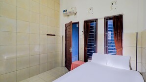 A hotel room with a bed, a small table, a wardrobe, and a window with curtains. - OYO Life 92841 Kos 88 (Perean Tengah)