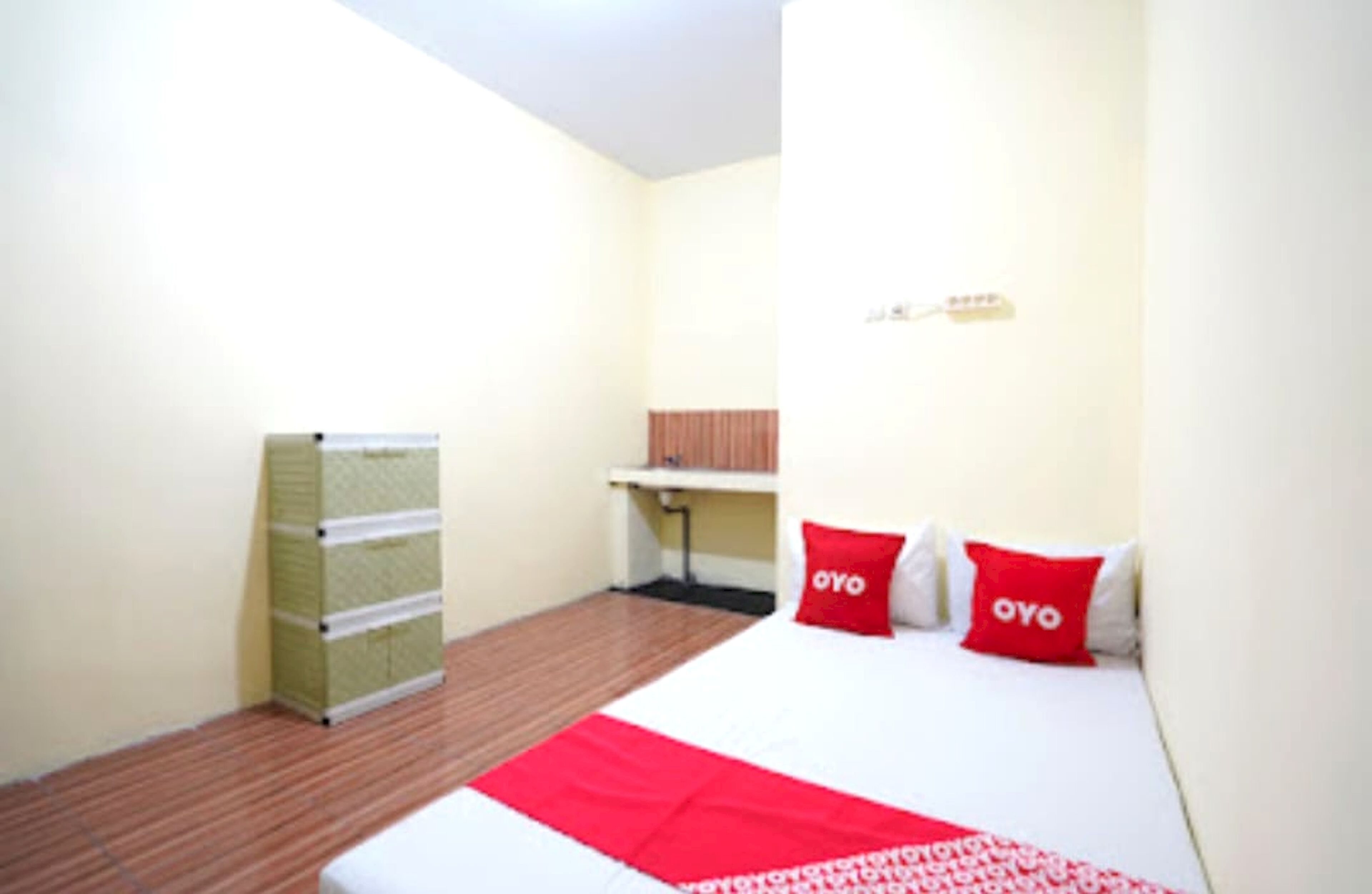 Hotelkamer met een bed, twee rode kussens, een rode deken, een houten vloer, een radiator en een klein tafeltje met een stoel.