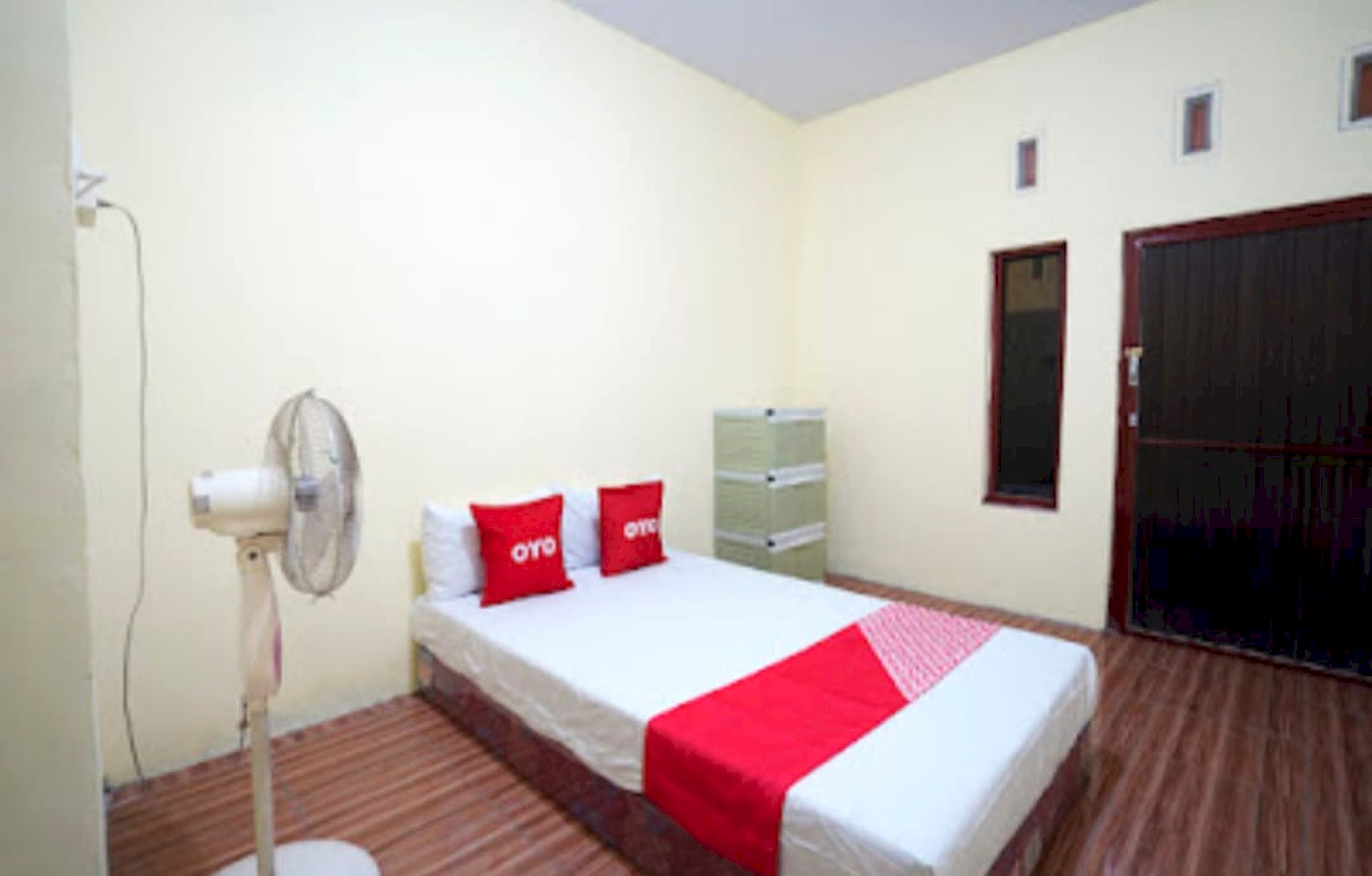 Una habitación con cama, ventilador, armario y un mueble pequeño.