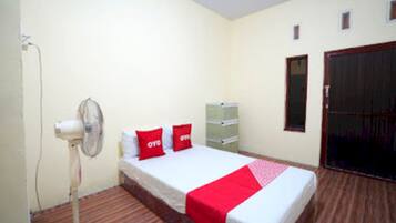 Una habitación con cama, ventilador, armario y un mueble pequeño.