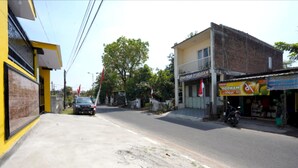 A street view with a yellow building on the left, a shop with a signboard on the right, and a parked motorcycle. - OYO Life 92920 Rumah Kost Azca (Sidoarjo)