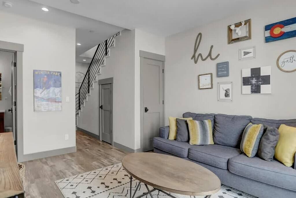 Un salon moderne avec un canapé gris, un tapis à motifs et un escalier menant à un autre niveau.