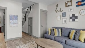 A modern living room with a grey sofa, patterned rug, and a staircase leading to another level.