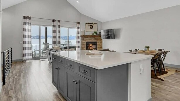 A modern kitchen with a large island, a fireplace, and a view through the glass door.