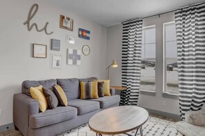 Un salon moderne avec un canapé gris, une table basse ronde et une grande fenêtre ornée de rideaux à rayures noires et blanches.