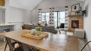 A modern living room with a fireplace, a dining area, and a view of the outdoors.