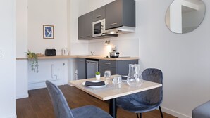 Une cuisine moderne avec des meubles gris, un four à micro-ondes et un évier. On y trouve une table à manger avec des chaises et un vase.