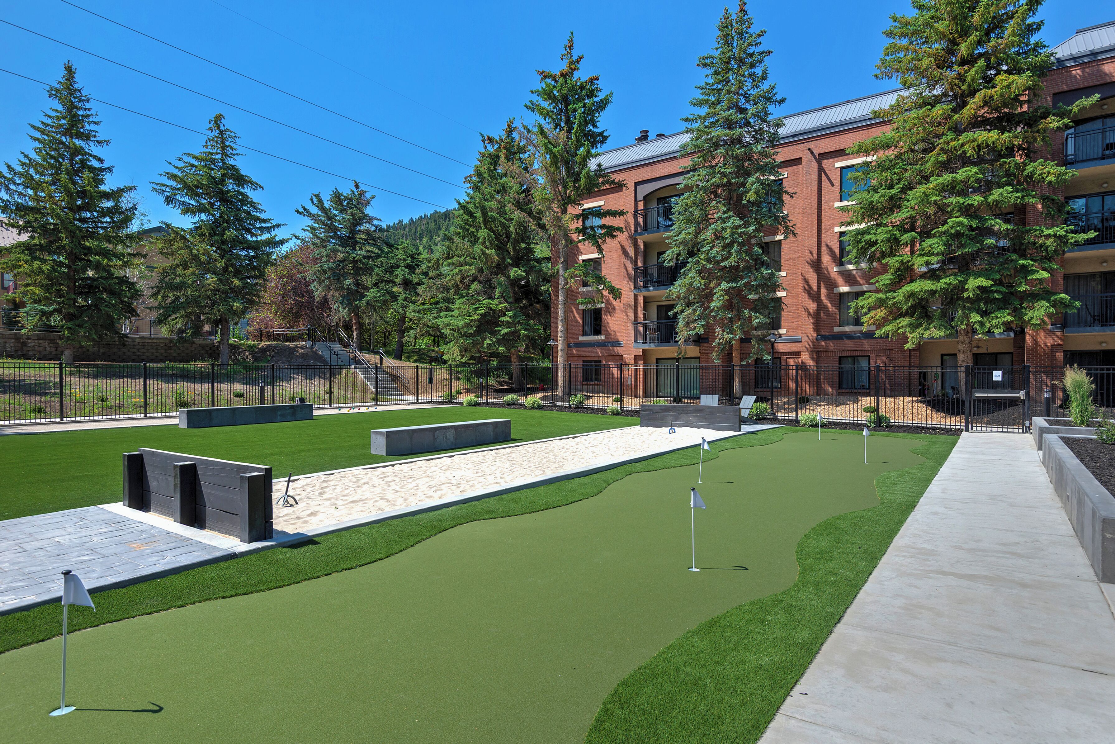 Un espace aménagé comprenant un green d’entraînement au golf, un chemin en béton et un bâtiment en briques doté de plusieurs balcons.
