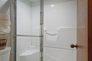 A glass-enclosed shower with a white bathtub, a towel rack, and a basket on the wall.