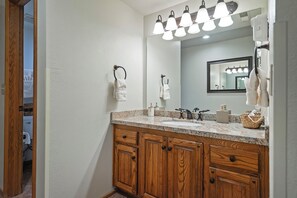 Un baño con armarios de madera, encimera de granito, un espejo y un perchero.