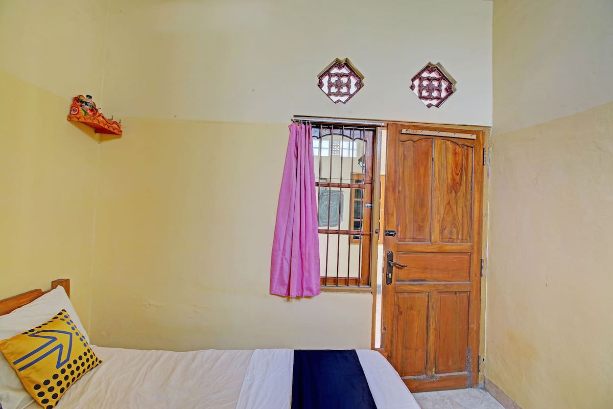 A bedroom with a bed, a wooden door, a window with a curtain, and a decorative wall piece.