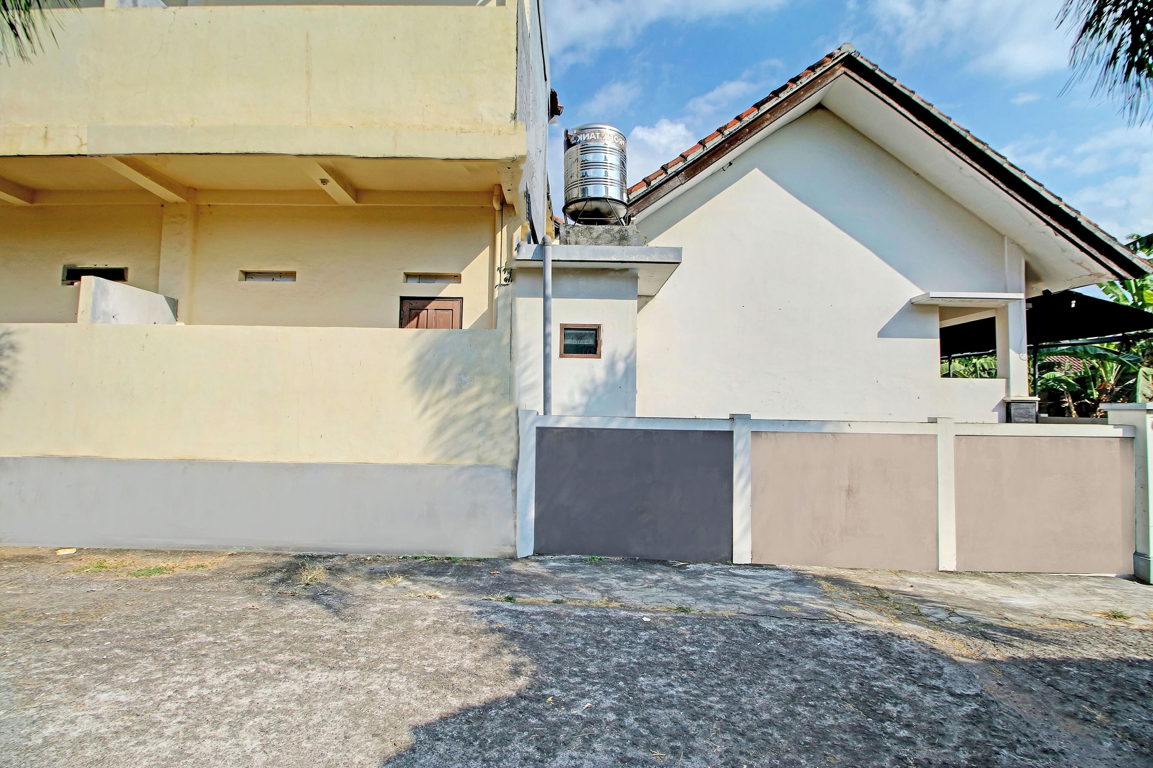 A two-story residential building with a flat roof, a water tank on the roof, and a gated entrance.
