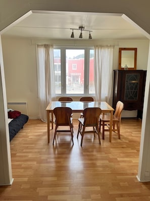 A dining area with a table and chairs, a window with curtains, and a view of a red building outside.