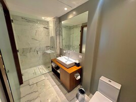 Un baño moderno con ducha envuelta en vidrio, tocador de madera con lavamanos y un inodoro.