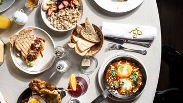 Una mesa de comedor con diversos platos de desayuno, cubiertos y vasos.