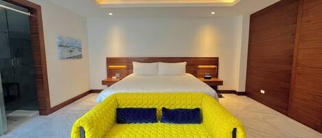 A modern hotel room with a large bed, a bright yellow armchair, wooden headboard, and a marble floor.