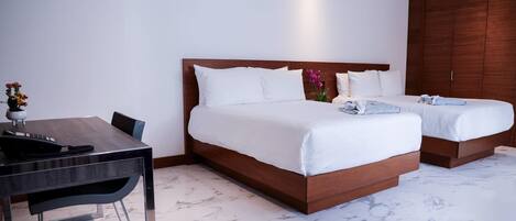 Una habitación de hotel con una cama grande, una cama más pequeña, un escritorio con una silla y un armario.