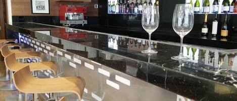A modern bar area with wooden bar stools, a black countertop, and a display of wine bottles.