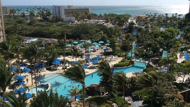 Un complexe hôtelier doté de plusieurs piscines, de palmiers et de parasols de plage.