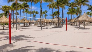 Un terrain de beach-volley avec un filet, entouré de palmiers et surplombé de parasols en feuilles de palmier.