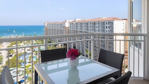Un balcon avec une table et des chaises en verre, donnant sur une plage et sur les bâtiments d’un hôtel.