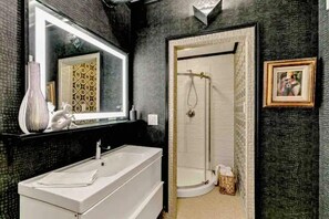 A bathroom with a large mirror, a white sink, and a shower area. - Carousel 2 - a proven location with a proven Host (Englewood)