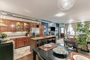 A modern kitchen with wooden cabinets, a dining area with a black table, and a living room with a sofa and a plant. - Carousel 2 - a proven location with a proven Host (Englewood)