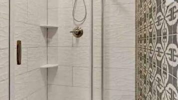 Una doccia a pavimento con porta in vetro curvo, un soffione e una piccola mensola.
