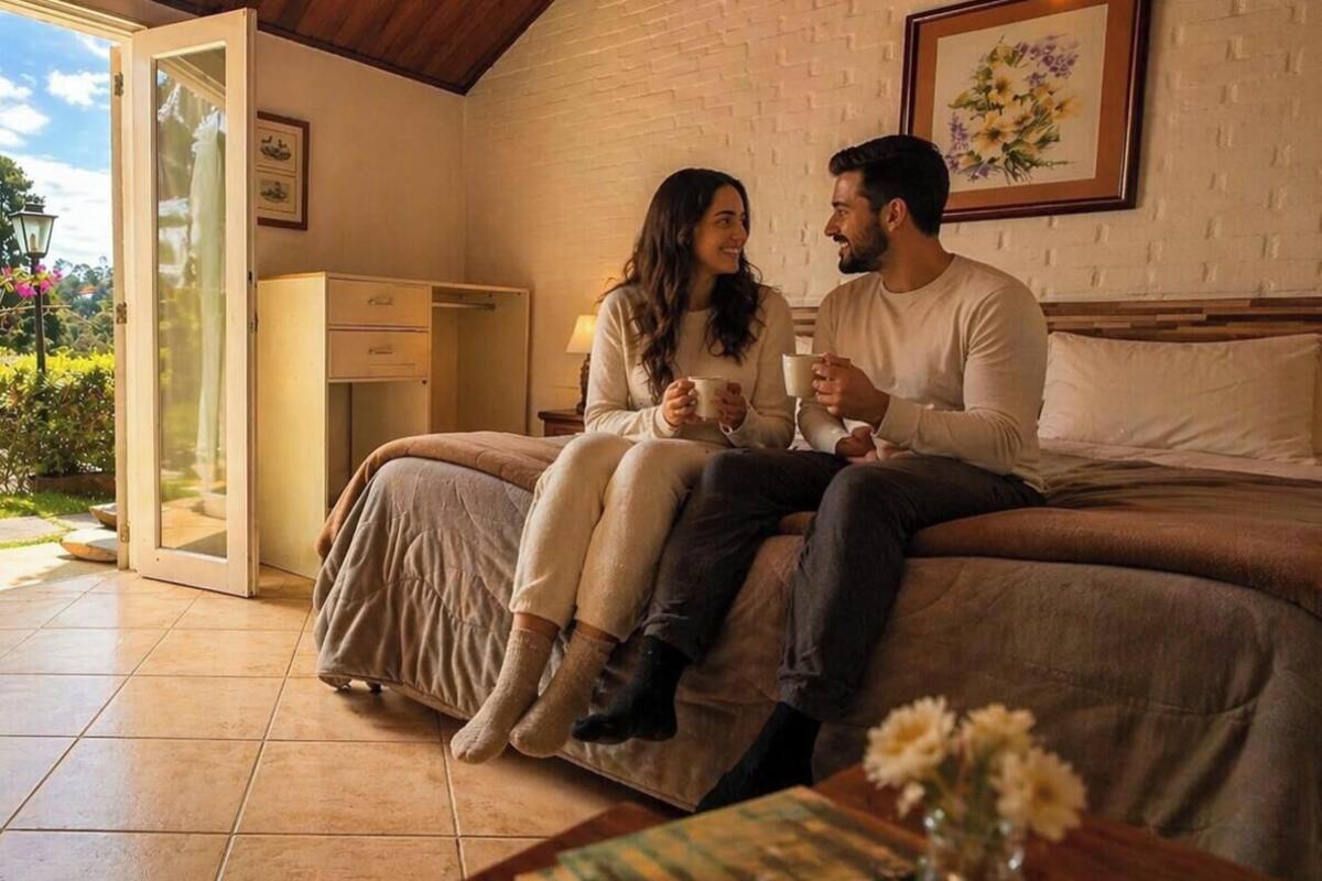 A couple sitting on a bed in a room with a sliding glass door, a small desk, and a framed picture on the wall.