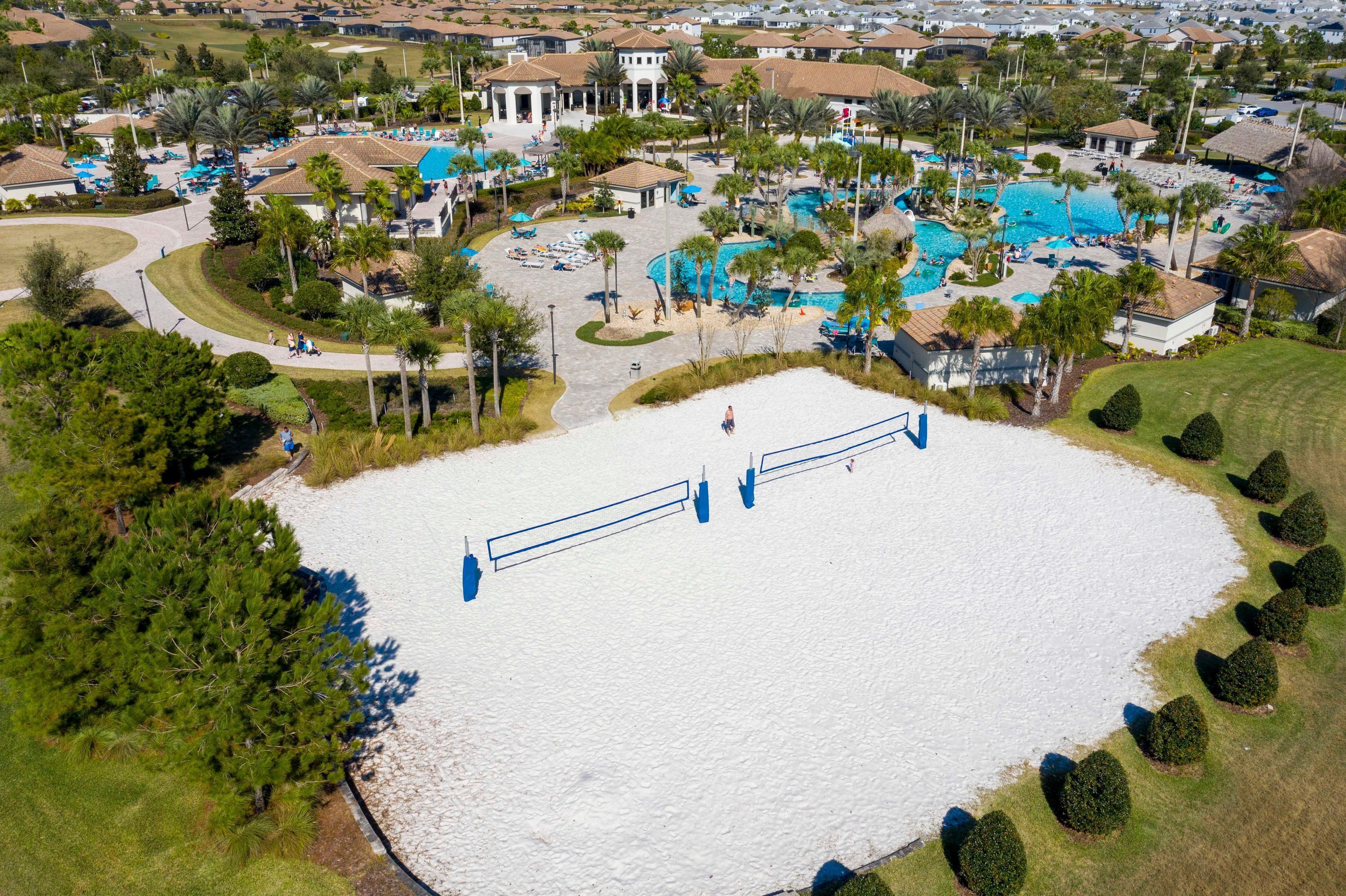 An aerial view of a resort with multiple swimming pools, palm trees, and a central white sand area.
