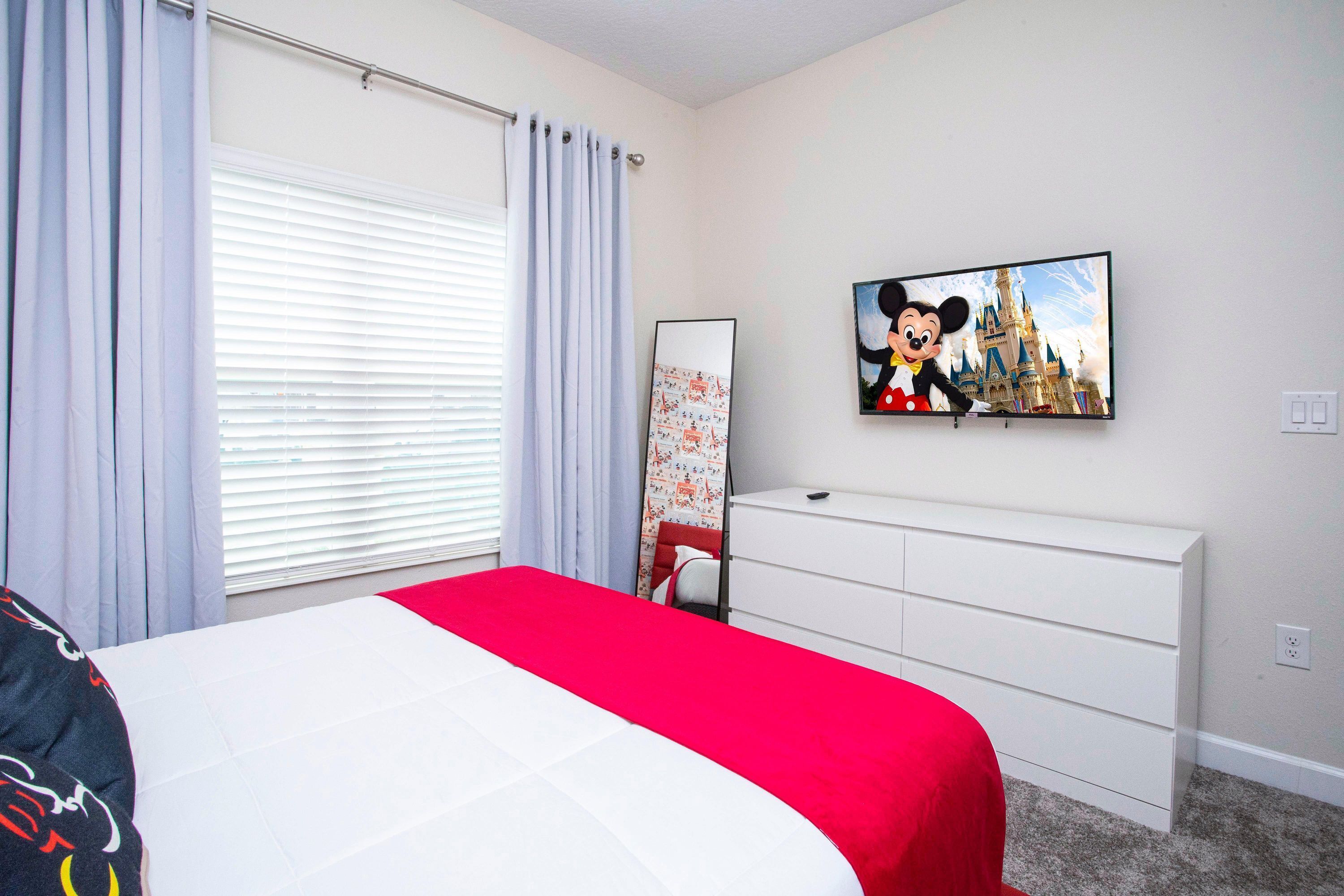 A bedroom with a bed, a dresser, a television, and a Mickey Mouse painting on the wall.