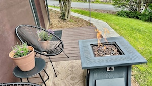En uteplats med en eldstad i metall, två stolar, en krukväxt och ett trädäck.