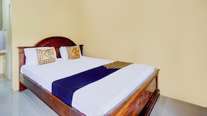 A single bed with a wooden frame, white bedding, and patterned pillows. - SPOT ON 93014 Griya Nautika Sukodono (Sidoarjo)
