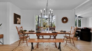 A dining room with a wooden table, chairs, a chandelier, and a floral centerpiece.