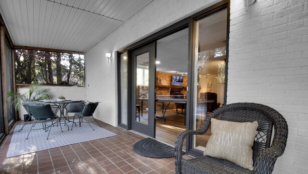 An outdoor patio area with a wicker chair, a dining table with chairs, and a view into the adjacent room.