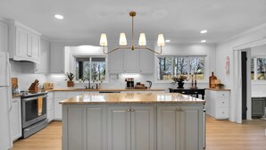 A spacious kitchen with a large island, white cabinetry, and a chandelier.