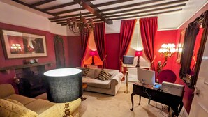 A living room with a sofa, a lamp, a television, a computer, and a red curtain. - Archway Guesthouse (Grantham)