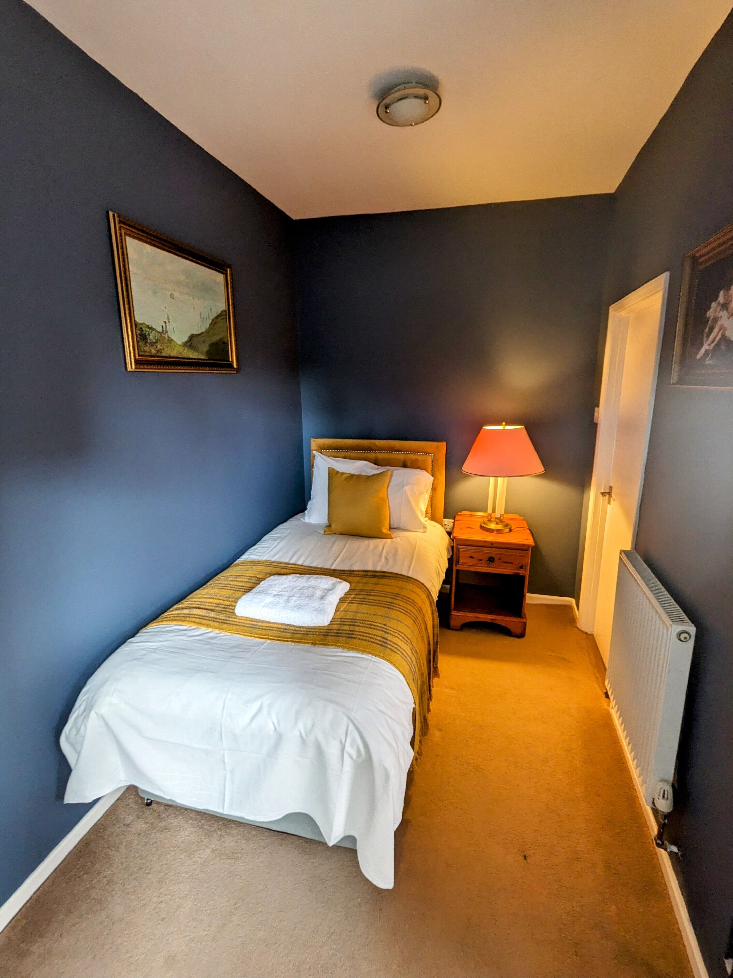 A bedroom with a bed, bedside table, lamp, and a radiator.