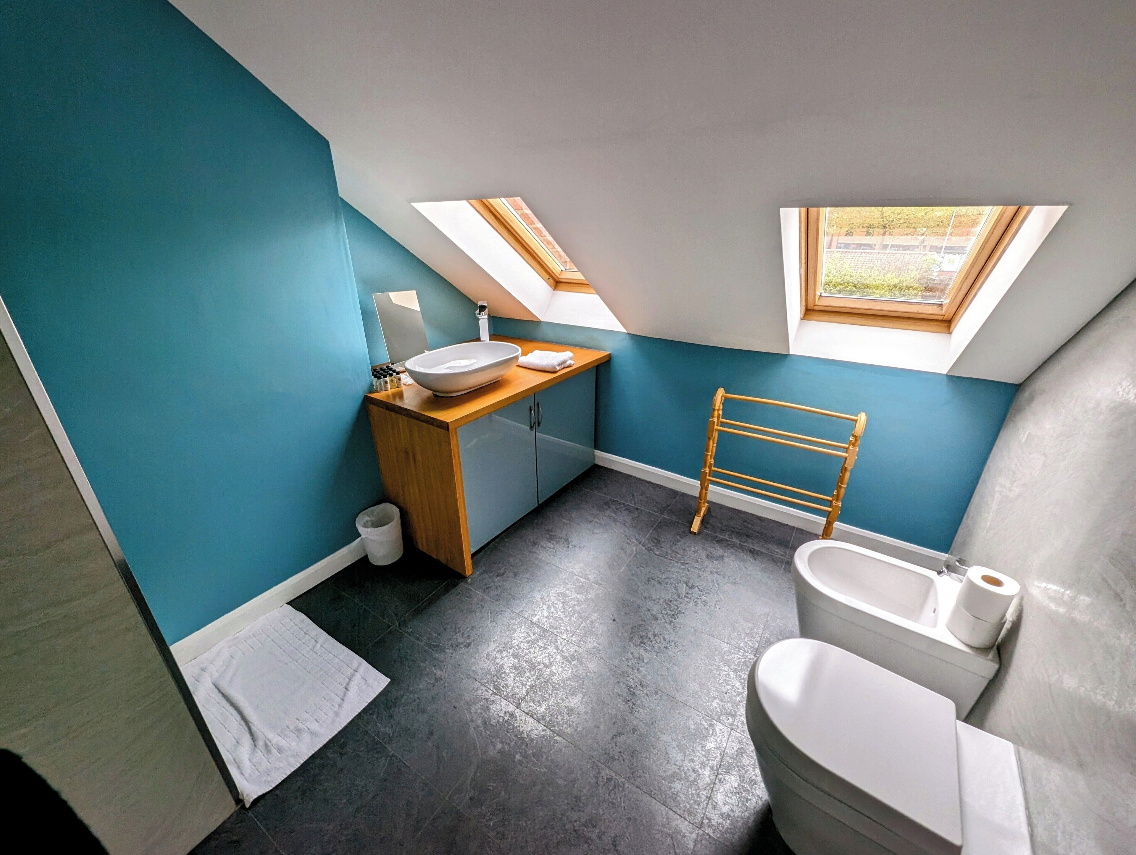 Ein kleines, modernes Badezimmer mit Dachfenster, einem Holzwaschtisch und einer Toilette.